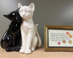 Black and white cat sculpture with small sign with cat platitude